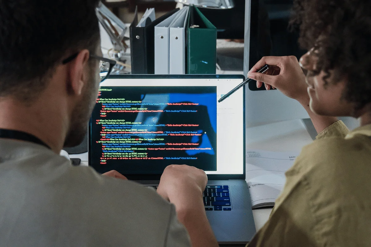 Two people focus on colorful code on a laptop screen.