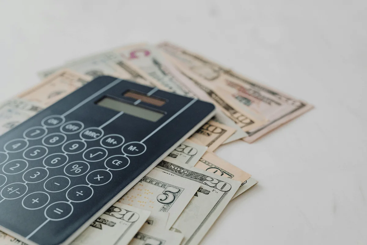 A black calculator rests on a fanned-out collection of various U.S. dollar bills on a light surface.