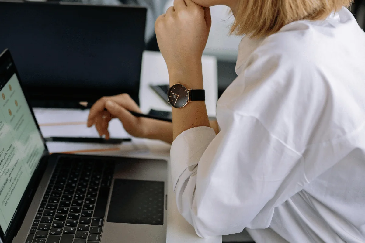 A person in a white shirt, wearing a black watch, is working on a laptop.