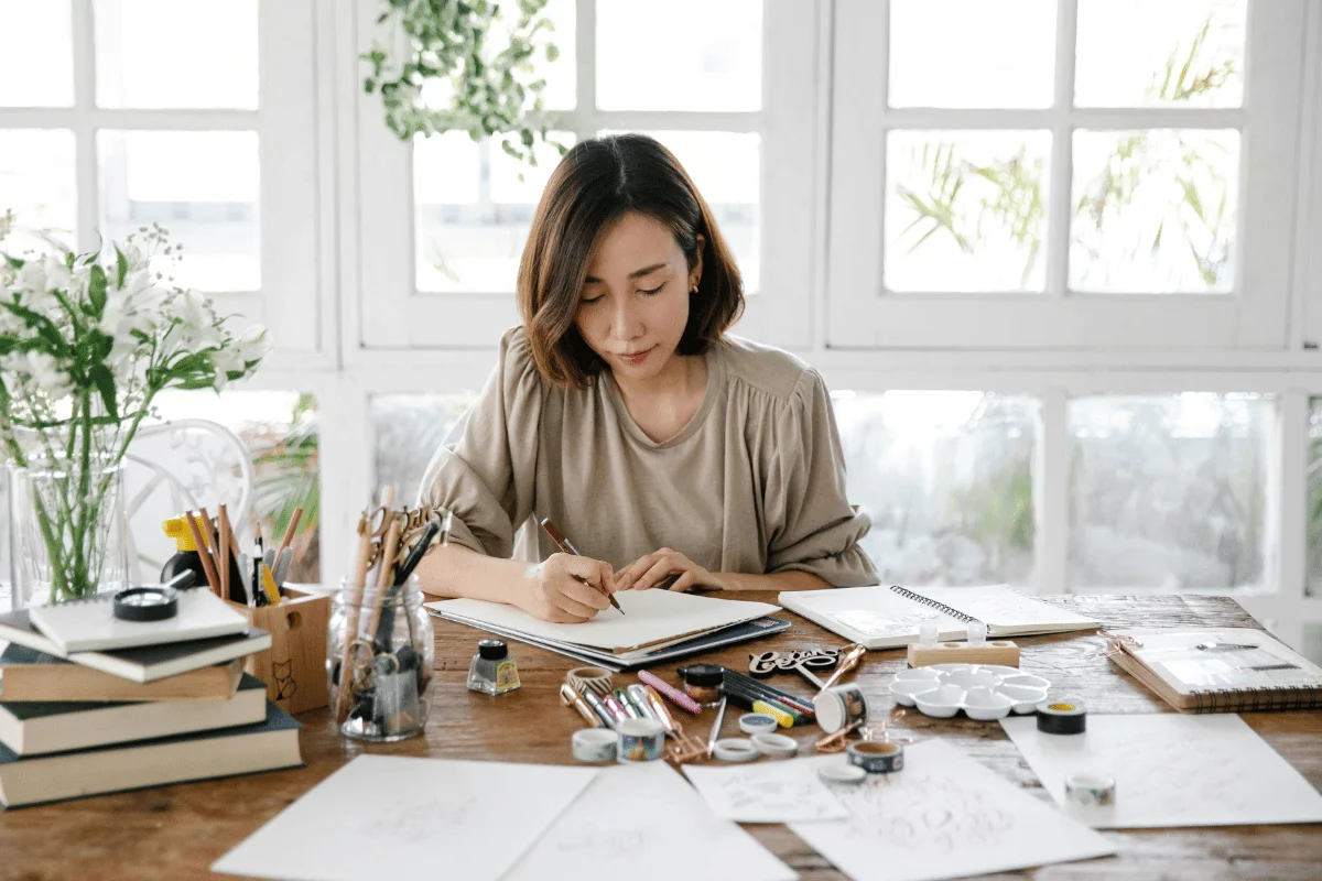 Woman working at creative desk with stationery and art supplies.
