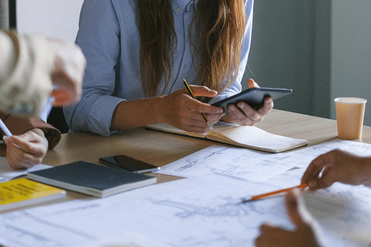 Person using a tablet while taking notes in a notebook at a desk.