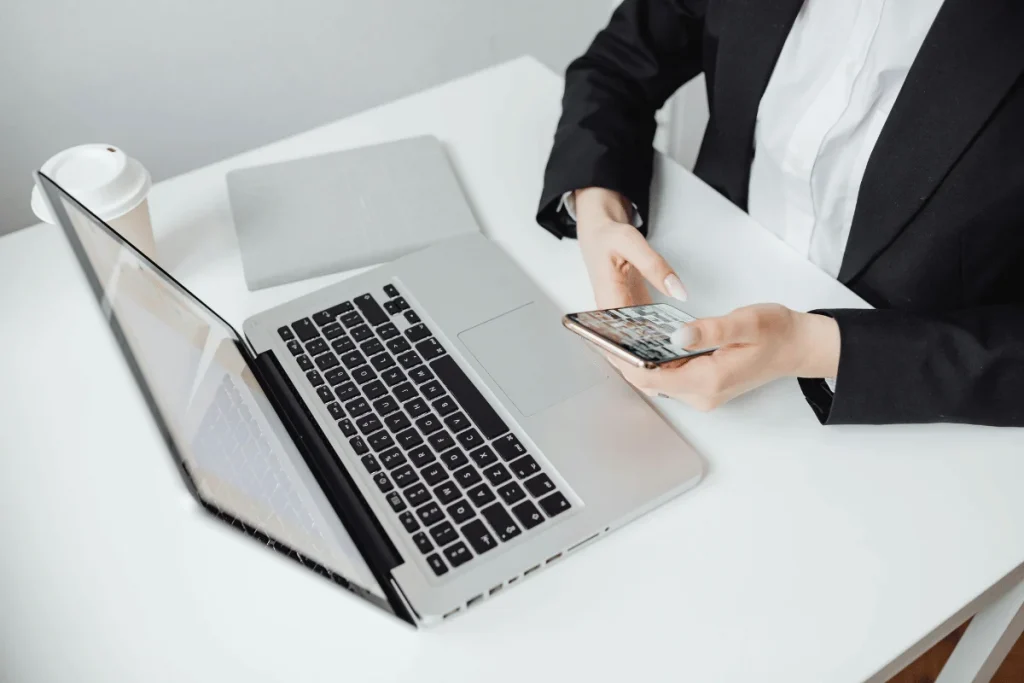 Business professional using a smartphone beside an open laptop on a clean desk.