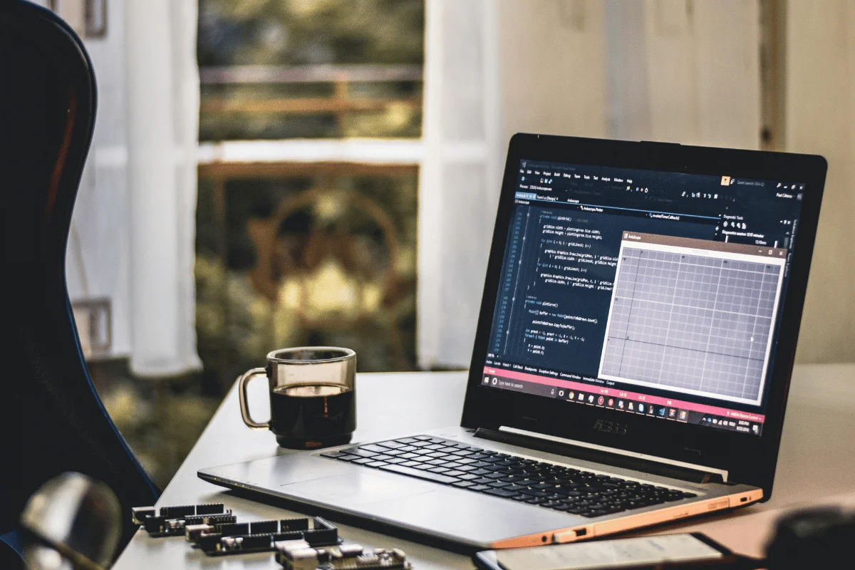 A laptop on a desk shows code on its screen, with a cup of coffee nearby.