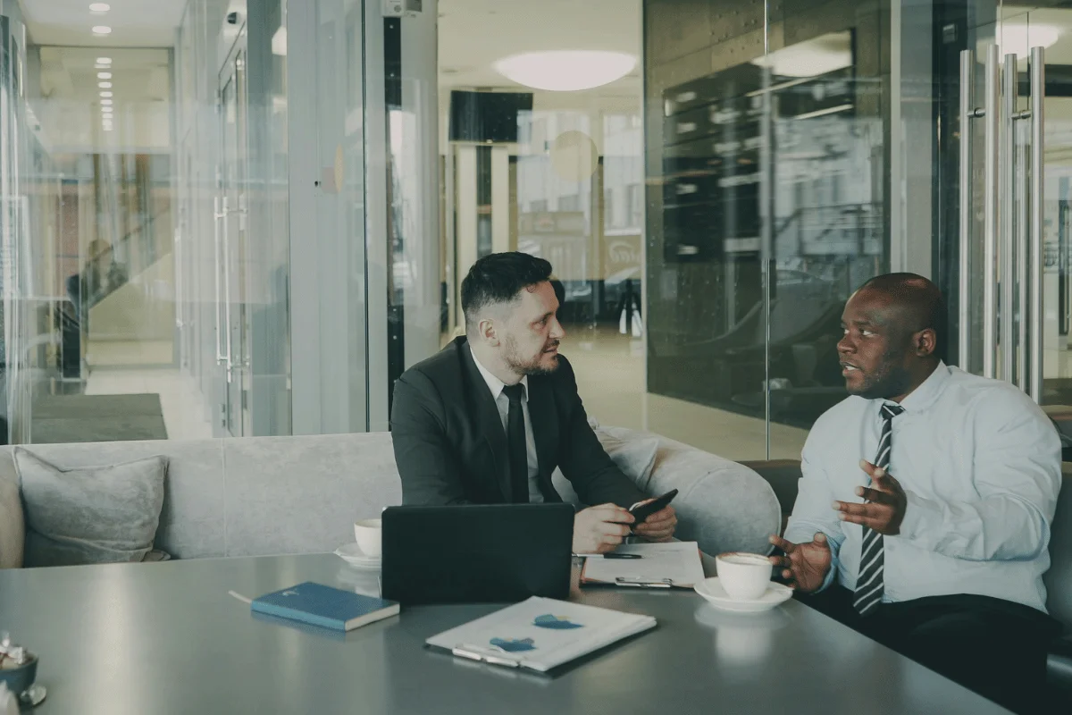 Two men in formal attire sit in a modern office, engaged in discussion.