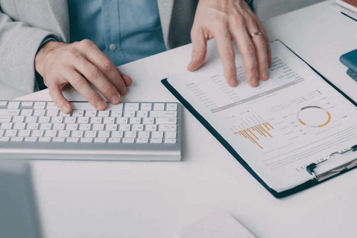 Office worker typing on a keyboard next to a financial report clipboard.