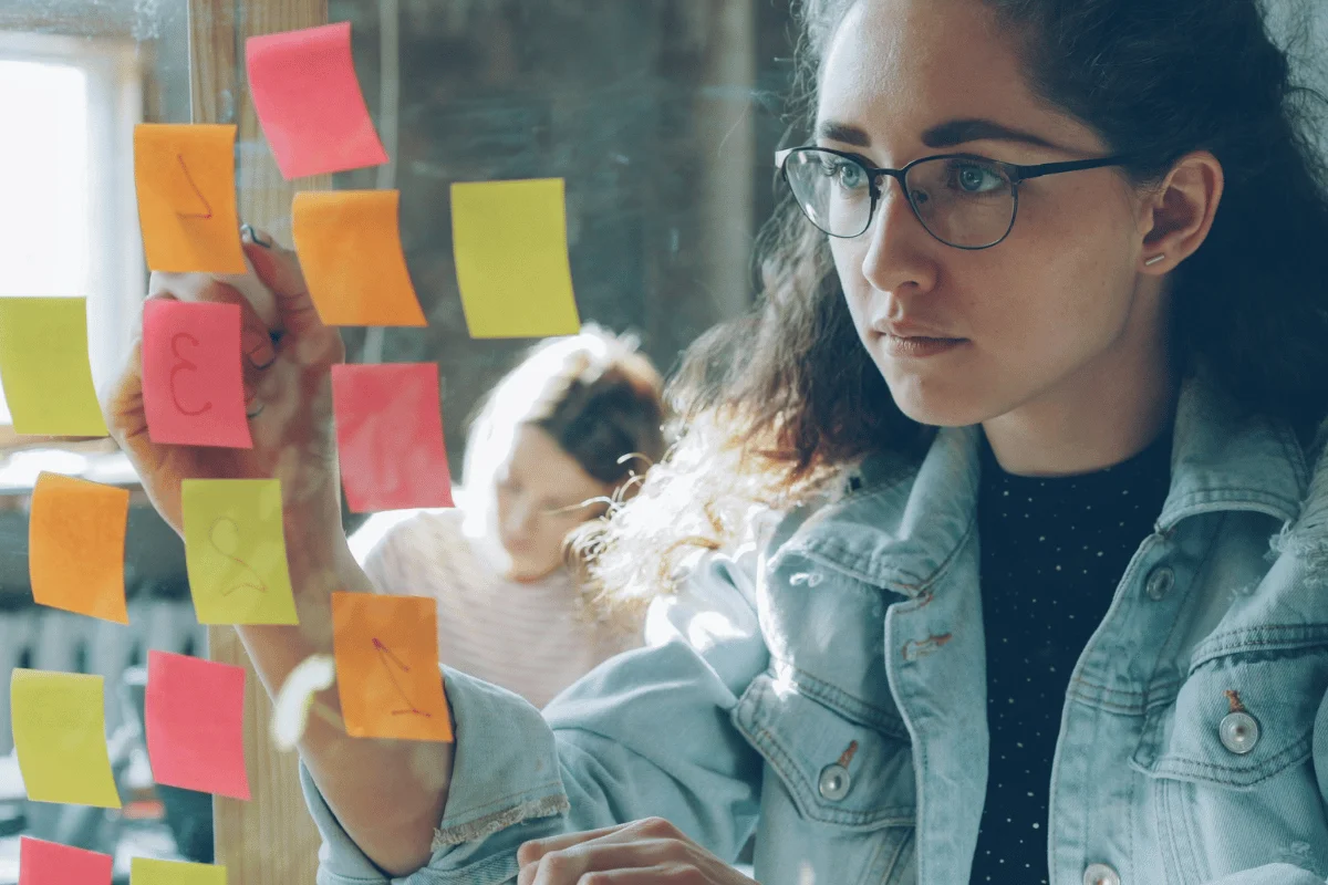 Professional placing sticky notes on a glass board during planning session.