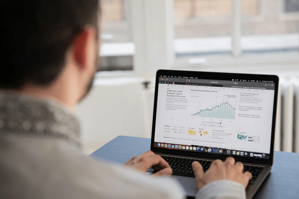 A person is working on a laptop displaying a graph and charts in a bright room.